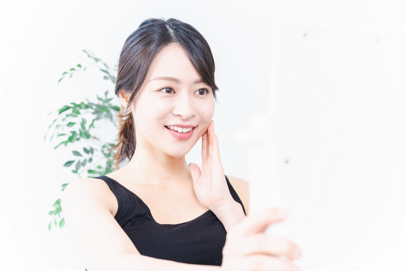 手鏡を見ながら頬に手を当てて微笑む女性