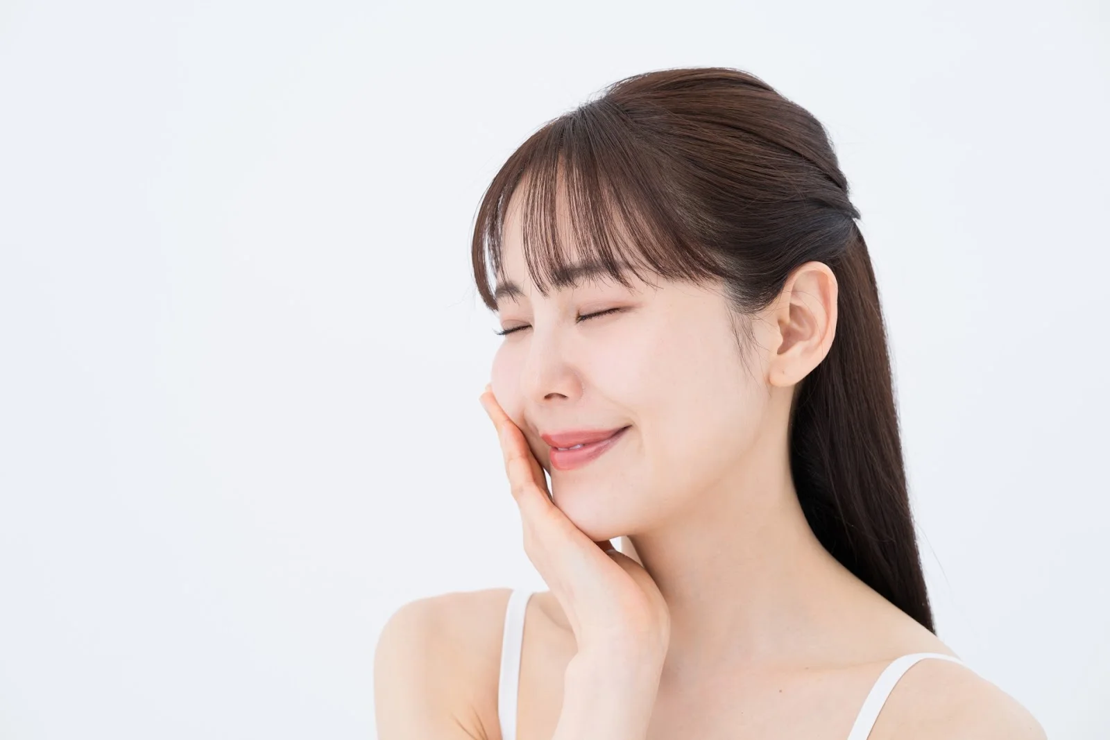 目を閉じて頬に手を添えてほほえむ女性