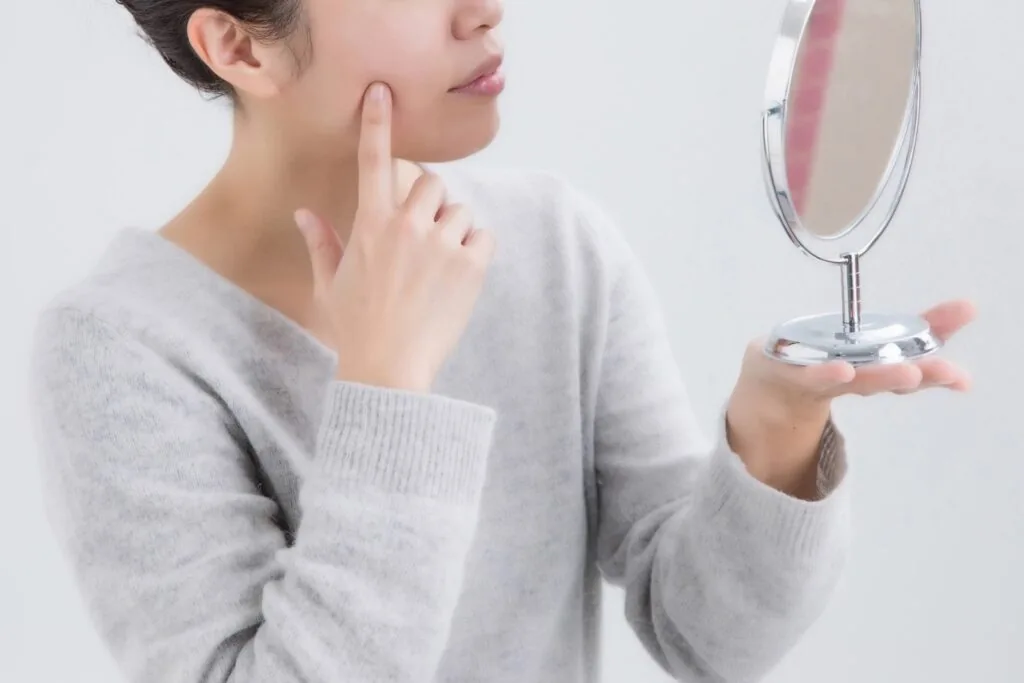 手鏡を見ながら頬に指を当てる女性
