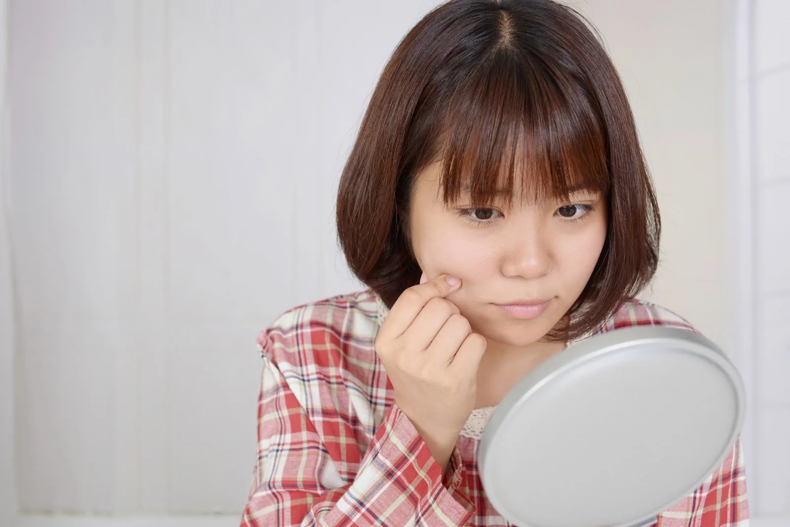 手鏡を見ながら頬の肌を気にする女性