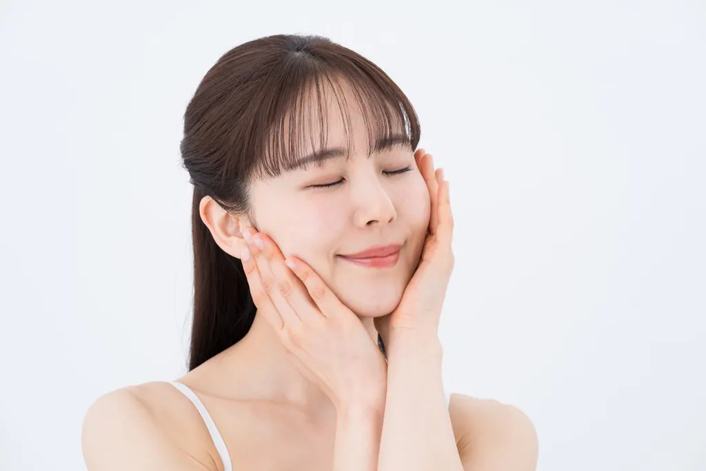 目を閉じて両手で頬に触れる女性