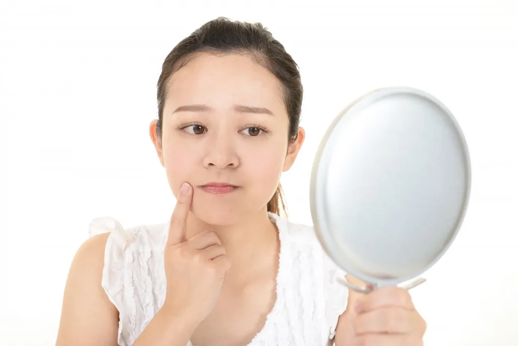 手鏡を持ち頬に触れる女性