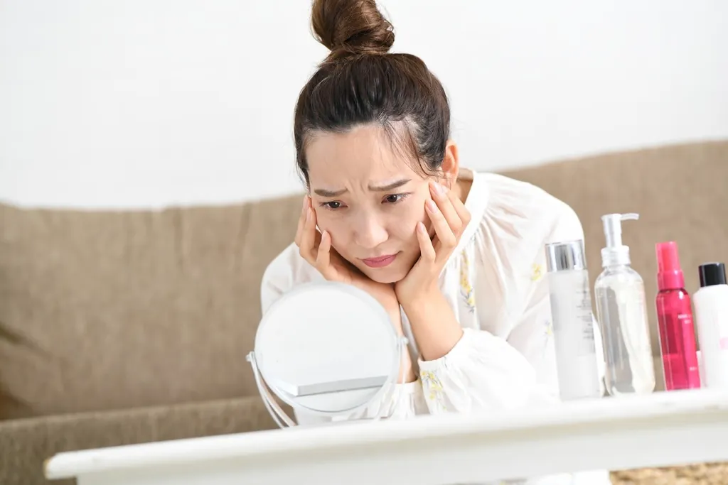 鏡の前で困った表情で頬に手を当てる女性