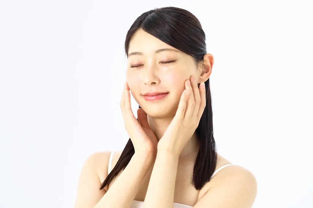目を閉じて両手で頬に触れる女性