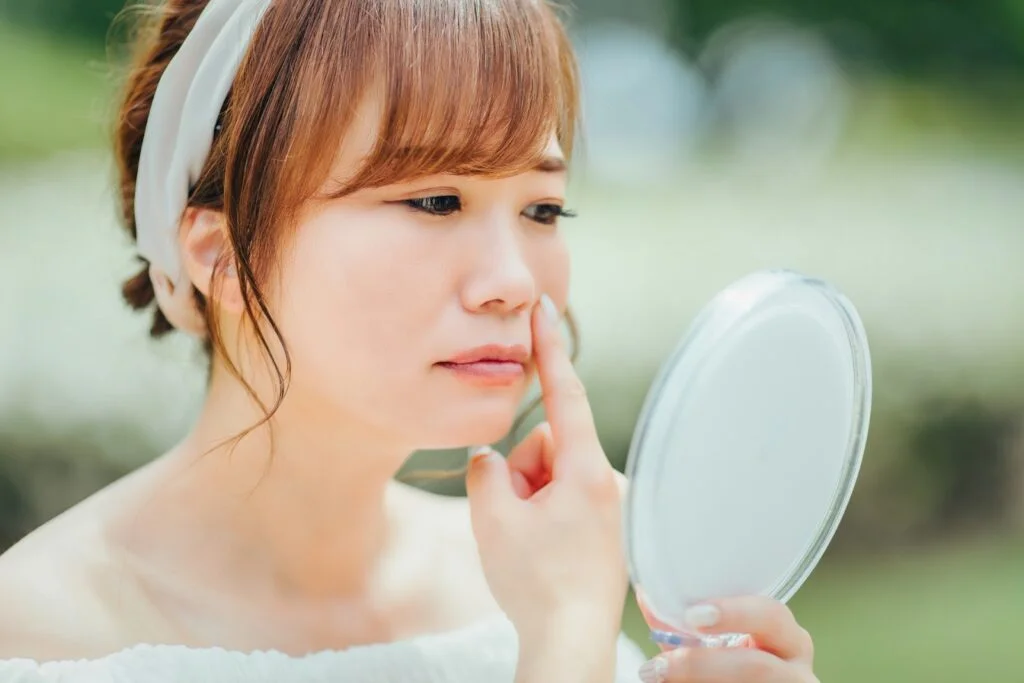 手鏡を見ながら鼻に指を当てる女性