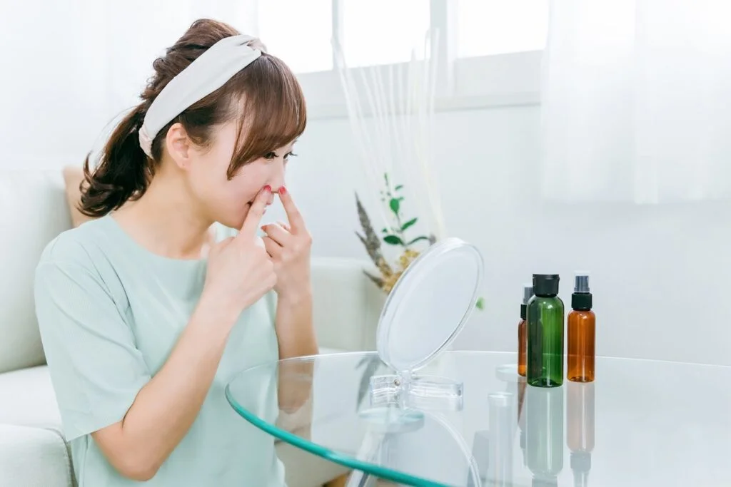 スキンケア用品を前に鼻に手を当てる女性