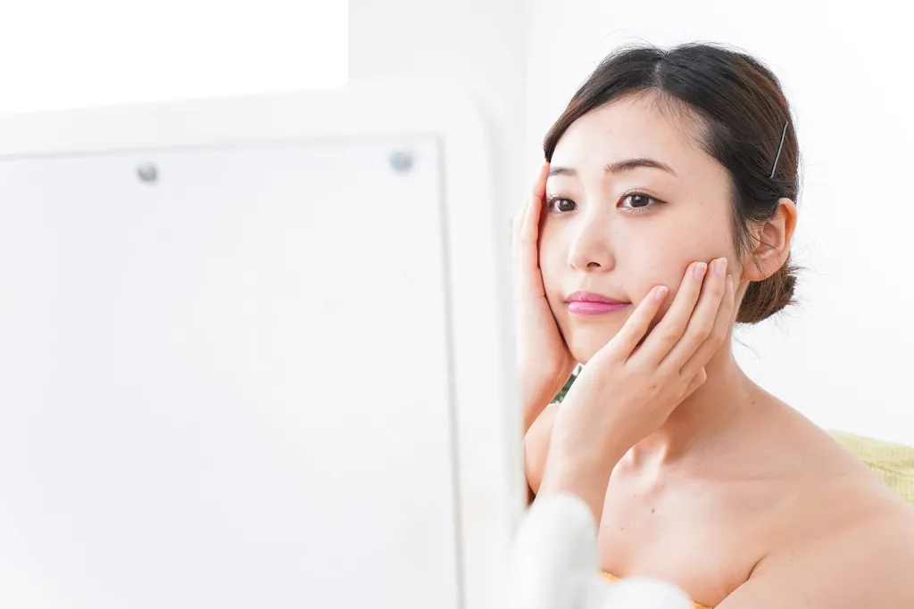 頬に両手を当てて鏡を見る女性