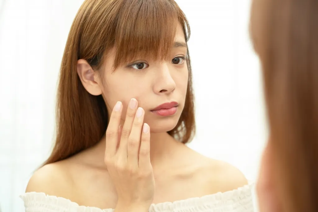 頬に手を当てて鏡を見る女性