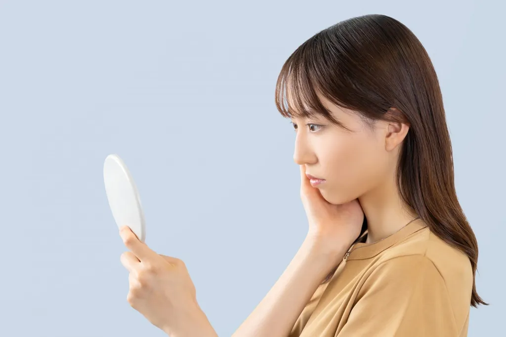 手鏡を見ながら頬に手を当てる女性