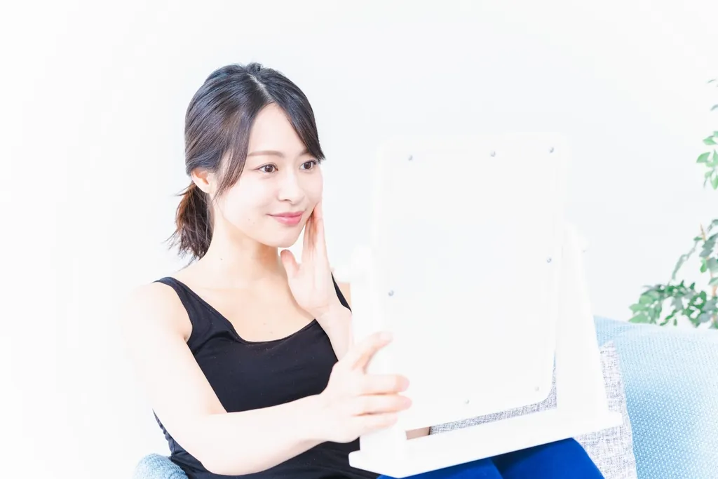 鏡の前で頬に触れてほほえむ女性