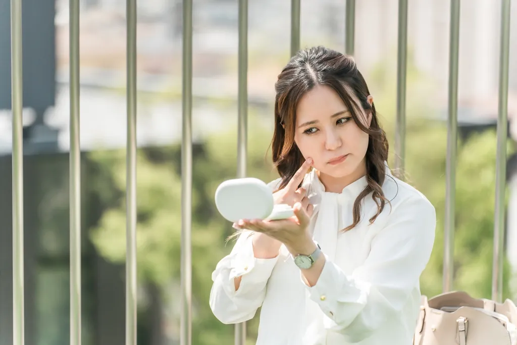 手鏡をのぞき込んで頬に触れる女性