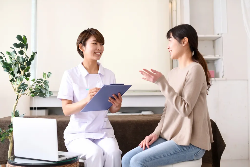 クリップボードを持つ白衣の女性と話す女性