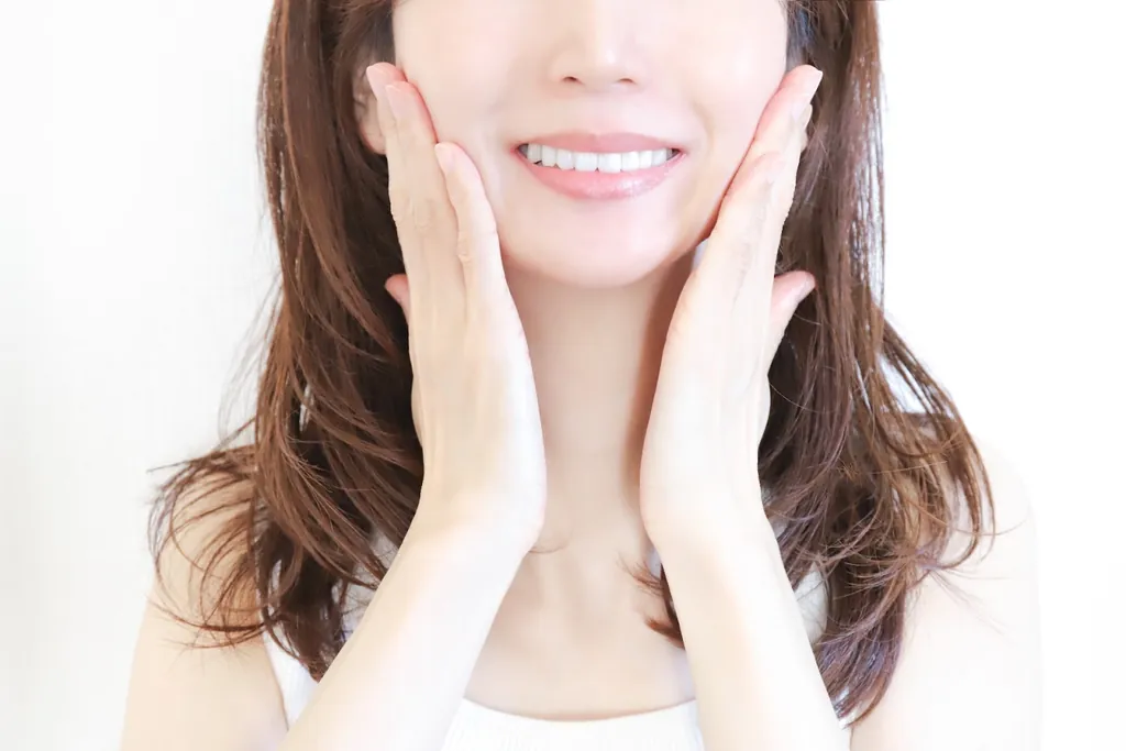 両手で頬を包んでほほえむ女性の口元