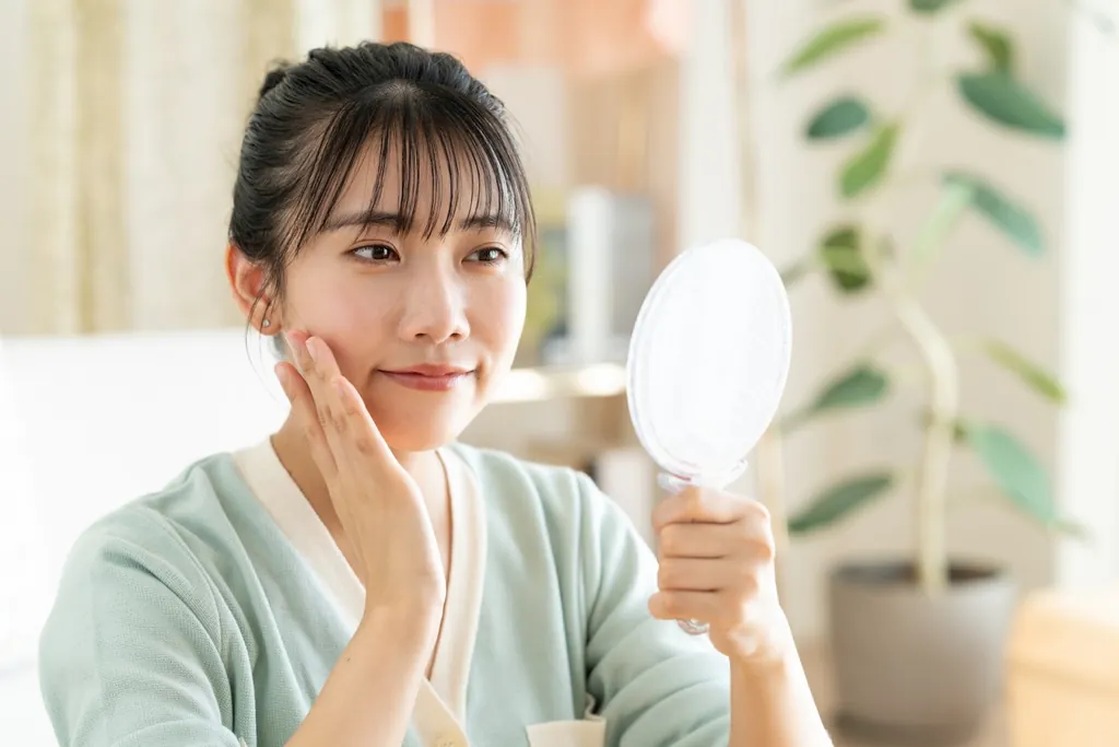 手鏡を見ながら頬に手を当ててほほえむ女性