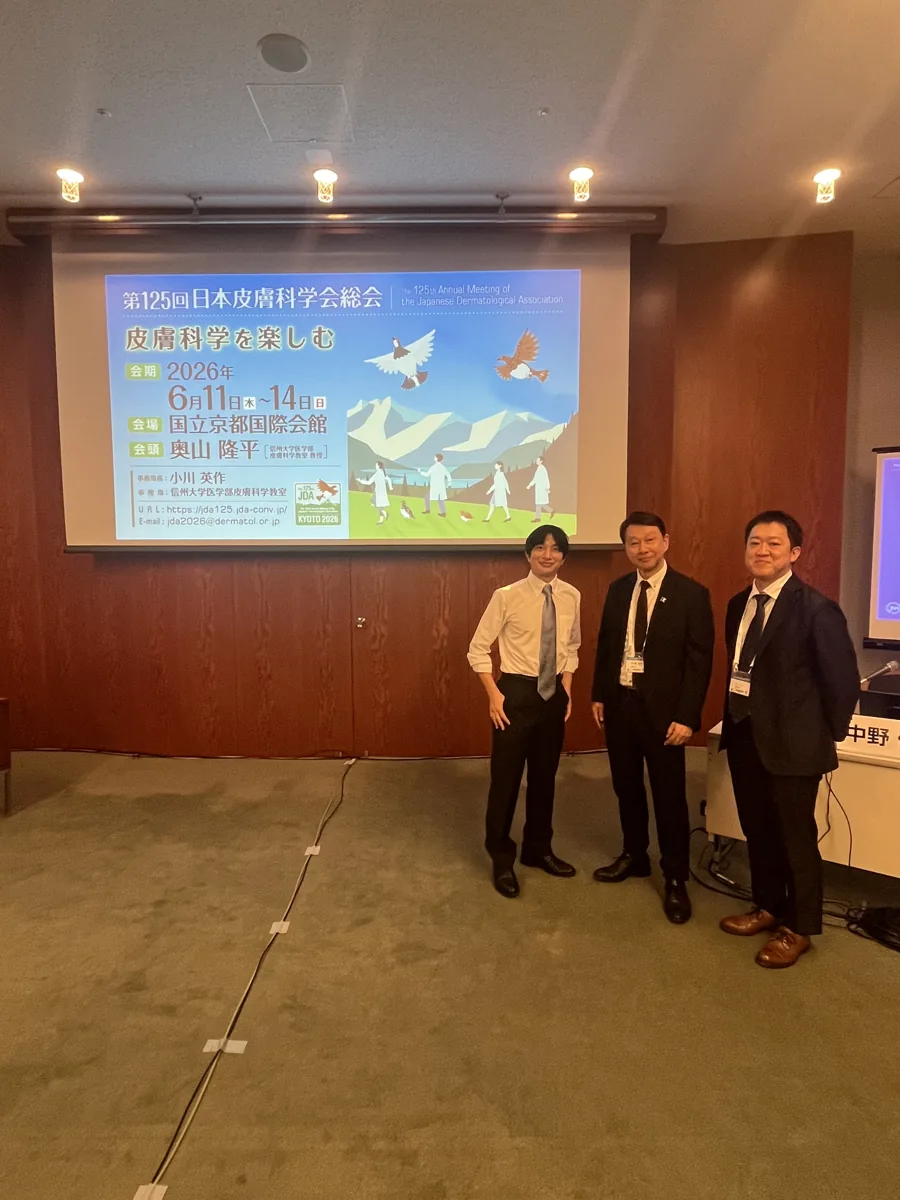 第125回日本皮膚科学会総会（2026年6月・国立京都国際会館）の会場で、ランチョンセミナーの司会・演者の先生方と並ぶ院長 野田真史